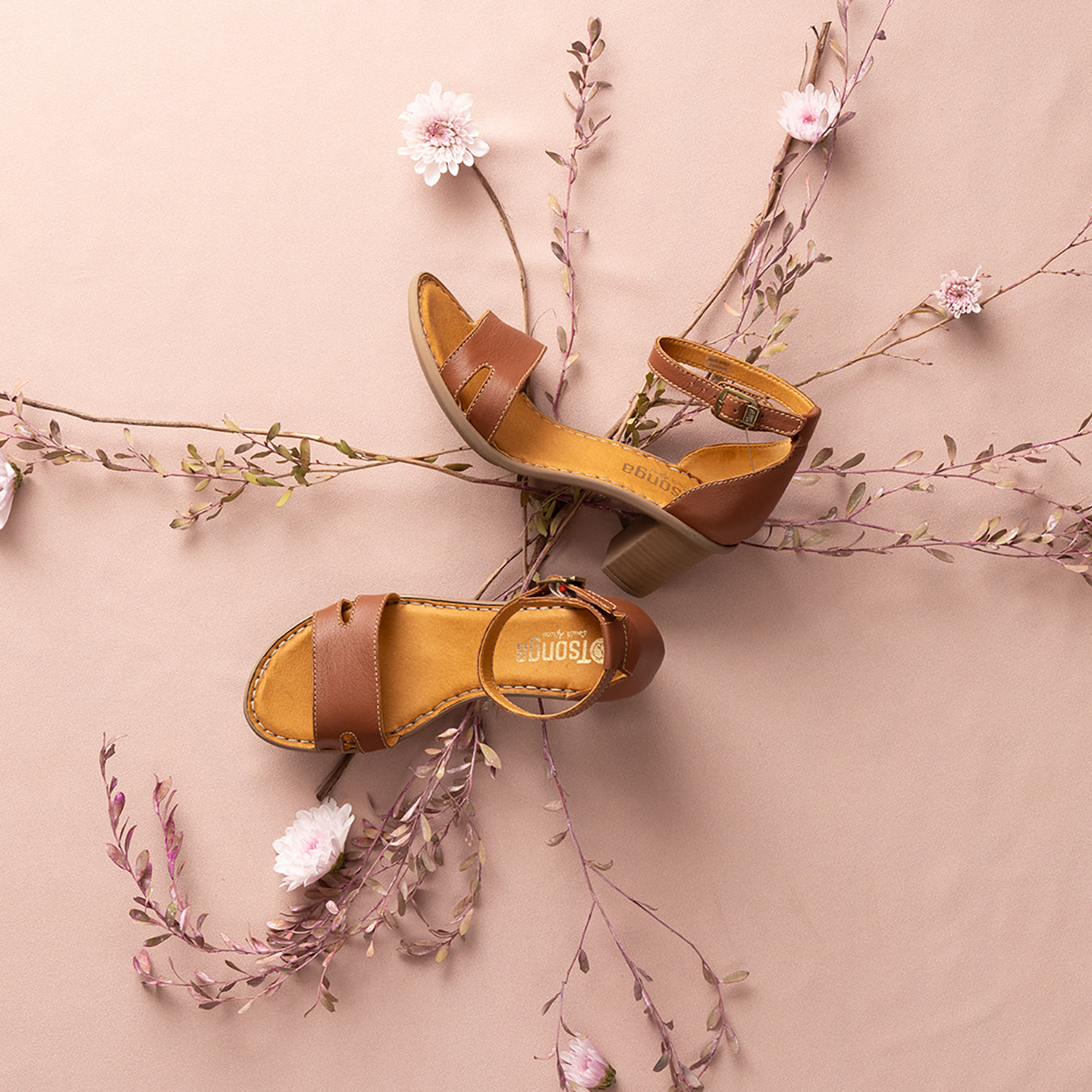 A pair of brown high-heeled leather sandals with adjustable straps and buckle closures, displayed on a light background with floral accents.