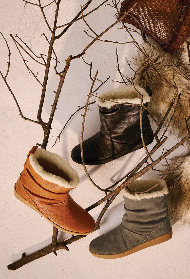 Three pairs of boots in brown, black, and gray on a branch against a neutral background