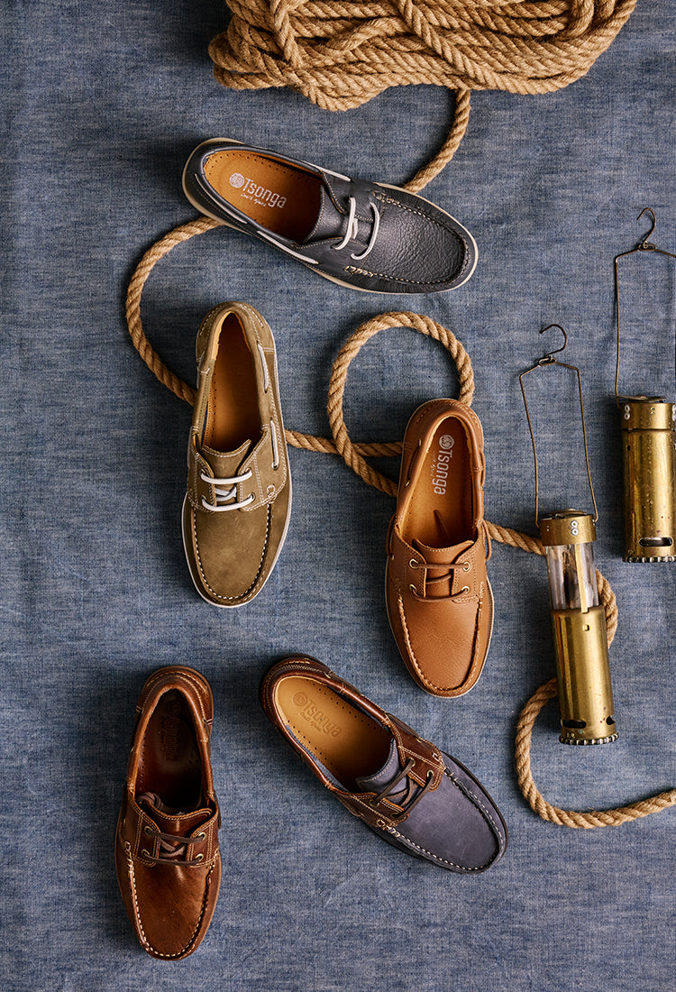 Brown, tan and navy boat shoes on a textured surface with rope and a lantern.