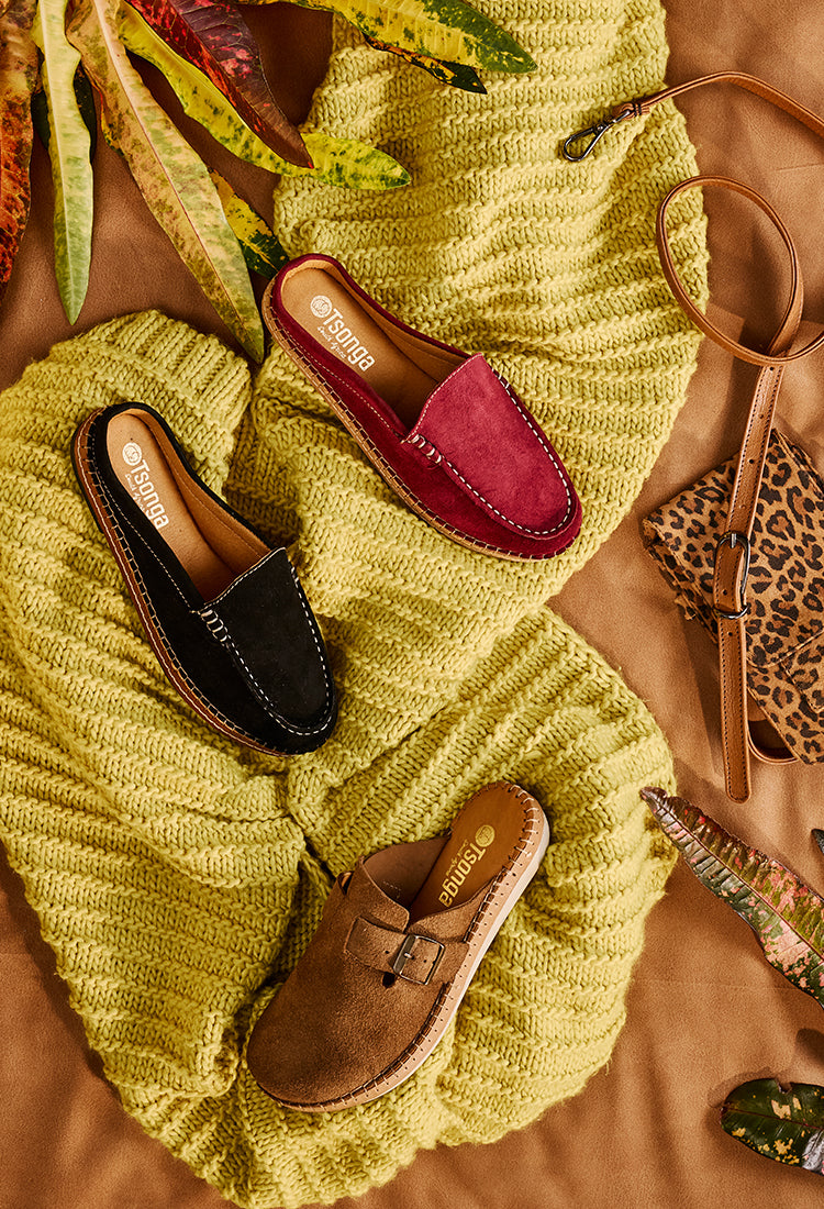 Three pairs of shoes on a textured surface with a handbag and leaves.