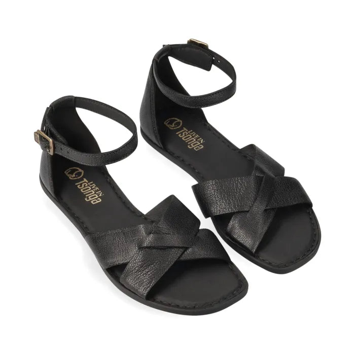 A pair of black leather flat sandals with crisscrossing straps across the toes, a slim ankle strap with a gold-tone buckle, and a low-profile sole, shown from above on a white background.