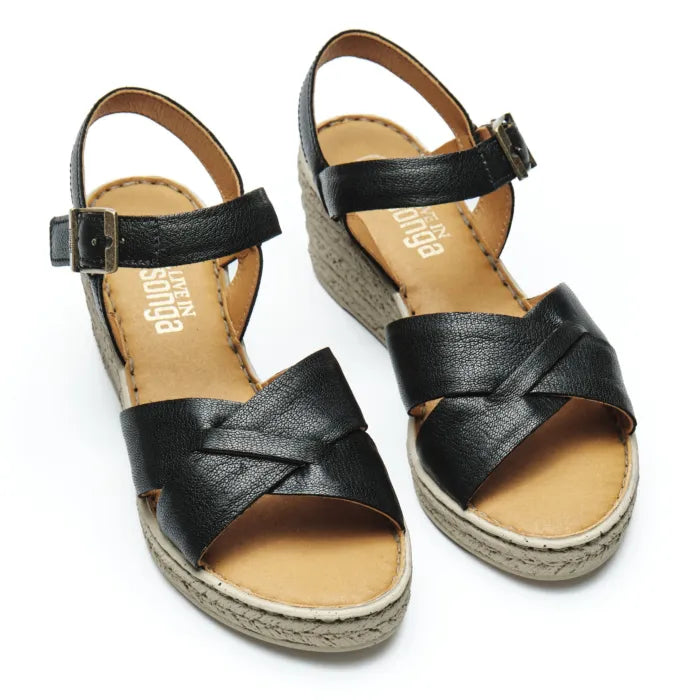 A pair of black leather wedge sandals with criss-cross front straps, adjustable ankle straps with buckles, and wedge soles. The insoles are tan and display the brand name 'Tsonga'.