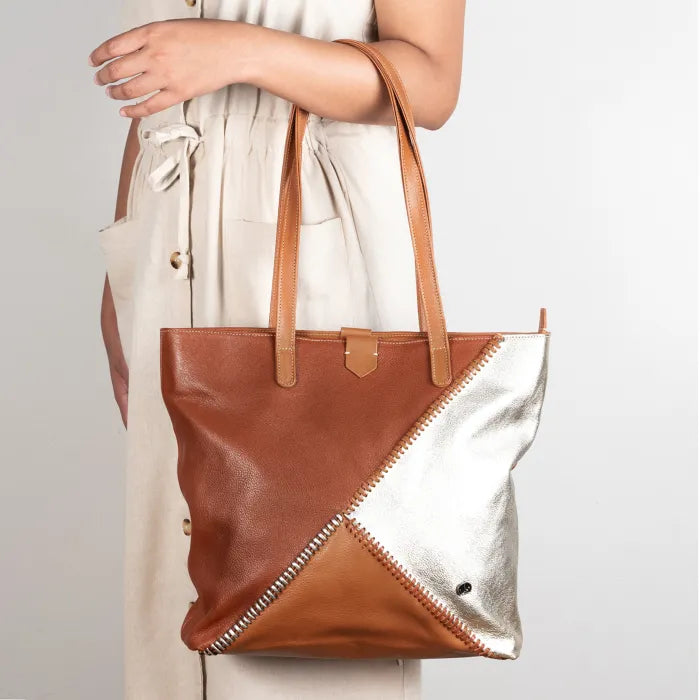 Brown and silver tote bag held by a person against a plain background