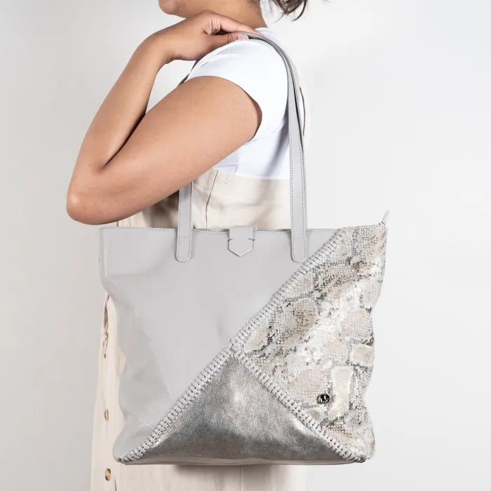 Person holding a grey tote bag with a decorative corner on a plain background