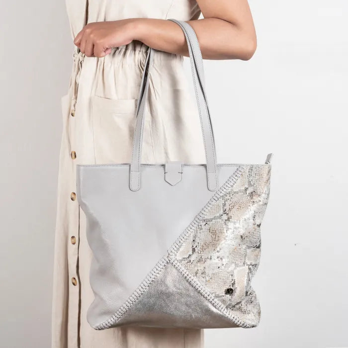 Person holding a light grey tote bag with a decorative pattern on a plain background