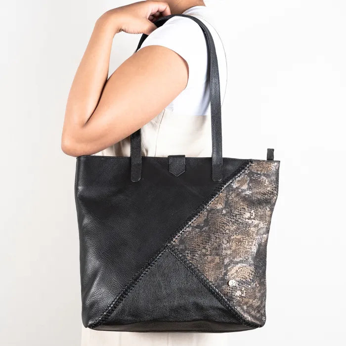 Black and metallic silver tote bag held by a person on a white background