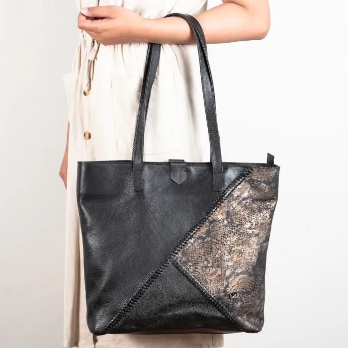 Black leather tote bag with metallic patch held by a person against a white background