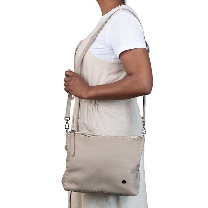 Person wearing a beige crossbody bag on a white background