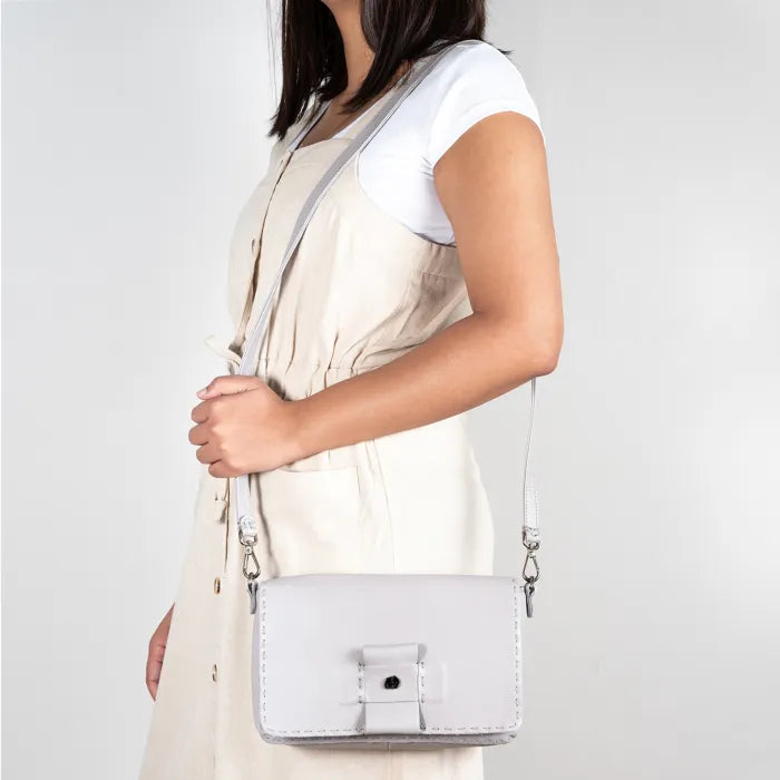 Person wearing a light grey crossbody bag on a plain background