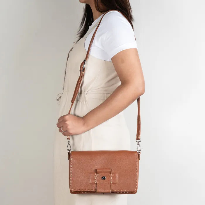 Person holding a brown leather crossbody bag against a plain background