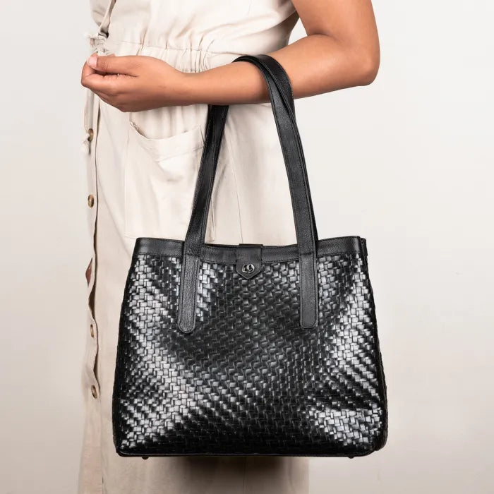 Black woven handbag held by a person against a neutral background