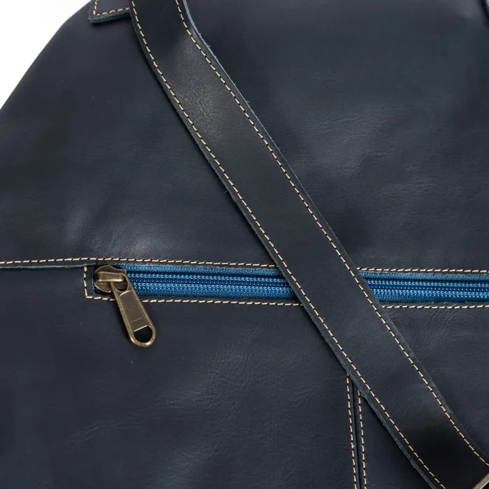 Close-up of a dark blue leather bag with a blue zipper and brown leather strap.