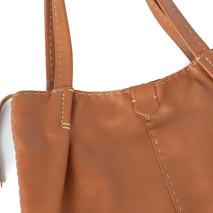 Close-up of a tan leather handbag with visible stitching on a white background