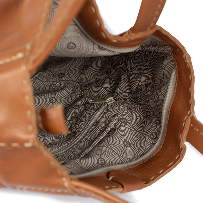 Close-up of a tan leather handbag with patterned interior on a white background