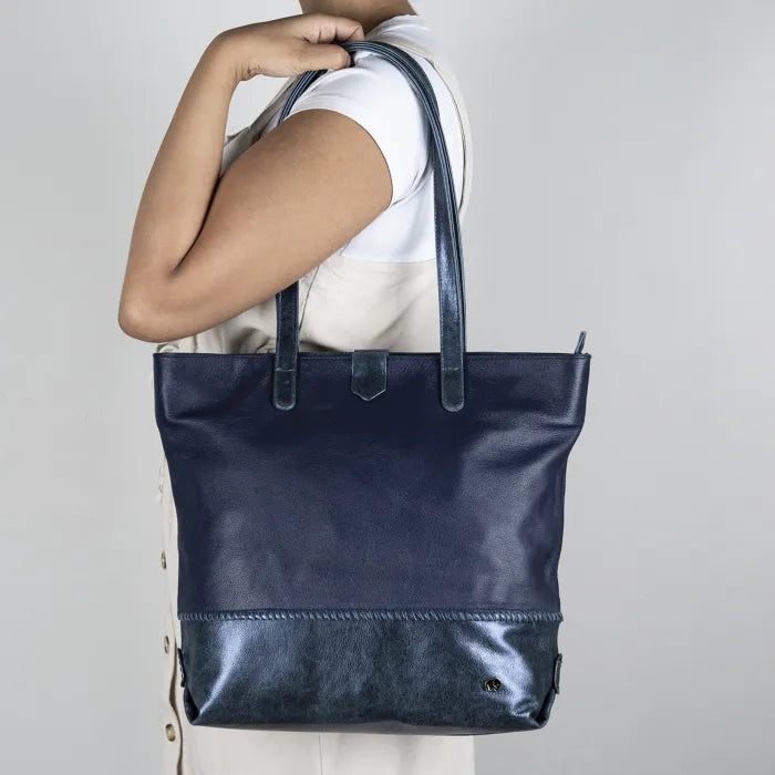 Person holding a navy blue leather tote bag against a plain background