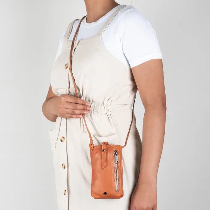 Person wearing a brown leather crossbody cellphone pouch on a plain background