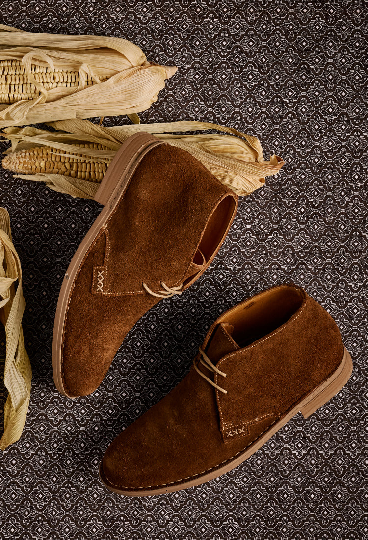 Brown suede shoes on a textured surface with corn husks.