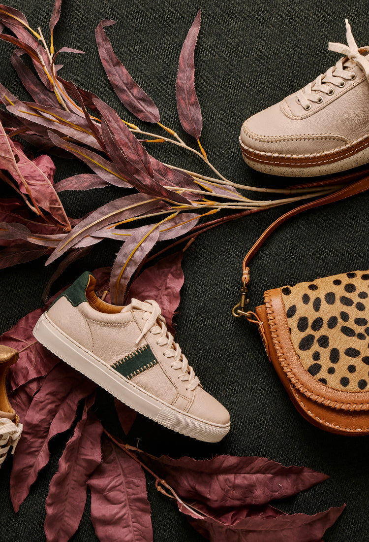 Pair of beige sneakers with a leopard print handbag on a dark surface with dried leaves.