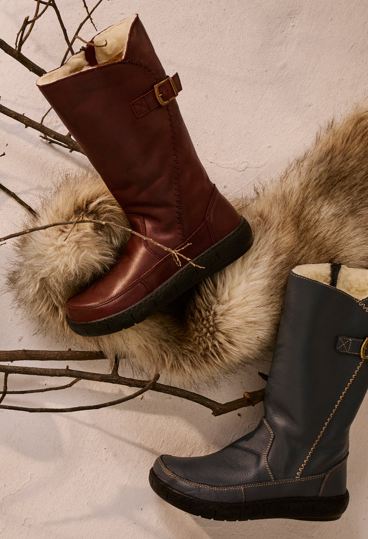 Brown and denim boots on a textured surface with fur and branches.