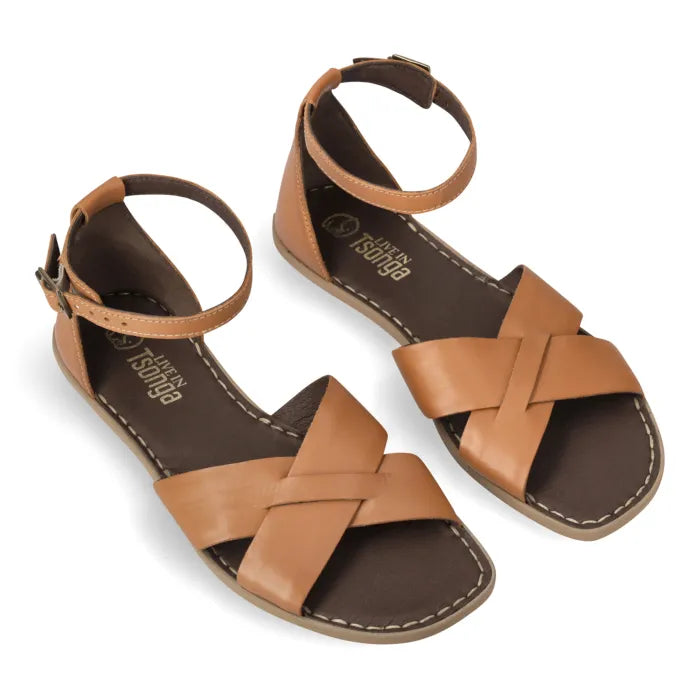 A pair of Tan leather slide sandals in a tan and dark brown colorway, featuring a criss-cross strap design and adjustable ankle straps, shown on a white background.