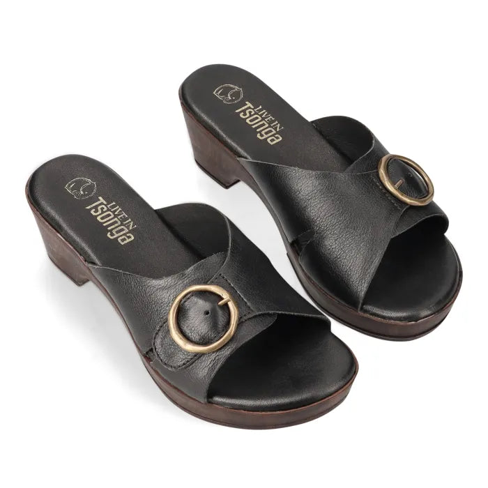A pair of black leather slide sandals with a low block heel and a circular gold-tone metal ring detail on the strap, shown on a white background.
