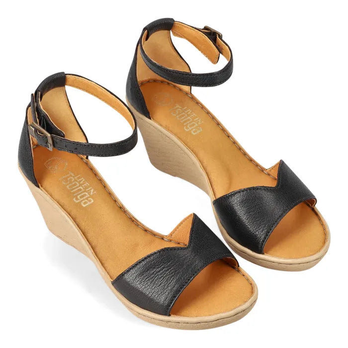 A pair of black leather wedge sandals with ankle straps and open toes, featuring a tan insole and a light brown wedge heel, shown on a white background.