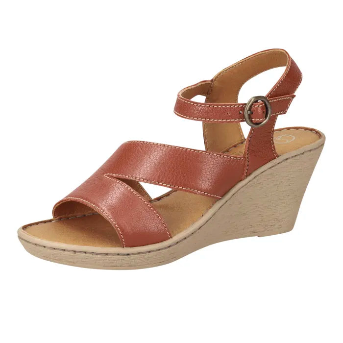 A women's wedge sandal with a terracotta brown pebbled leather upper, featuring crisscross front straps, an adjustable ankle strap with a silver-tone buckle, and a light beige wedge heel, shown against a plain white background.