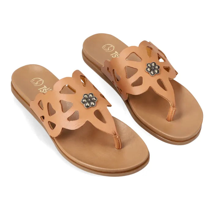 A pair of tan leather thong sandals with cutout details and a small silver flower charm on the strap, shown on a white background.
