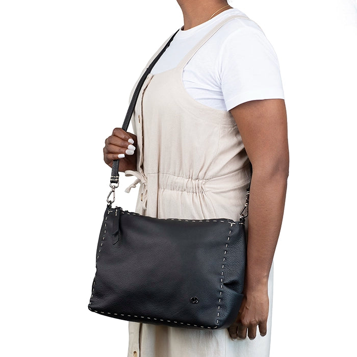 Person holding a black leather handbag against a white background