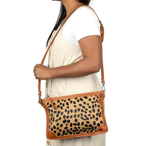 Person holding a crossbody bag with leopard print and tan leather accents.