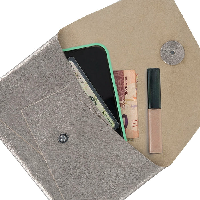 Open metallic silver leather clutch displaying contents including a smartphone, money, ID cards, and lip gloss, with beige suede interior and front pocket.