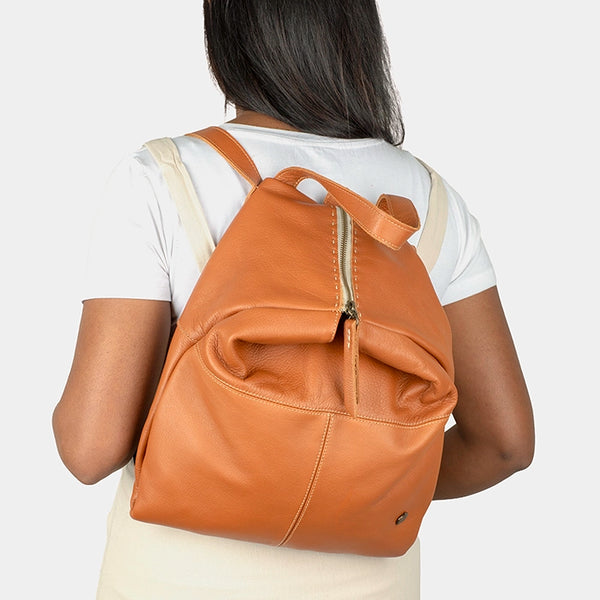 Person wearing a tan leather backpack on a plain background