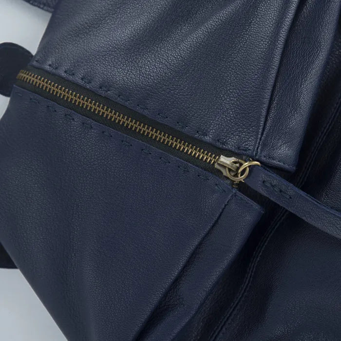 Close-up of a navy blue leather bag with a gold zipper on a light gray background