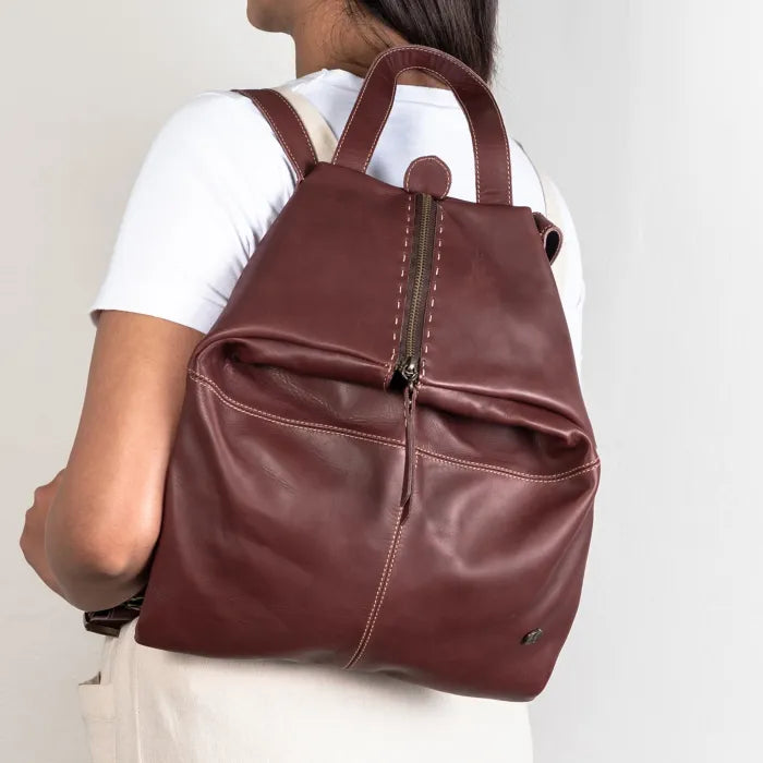 Maroon leather backpack worn by a person on a plain background