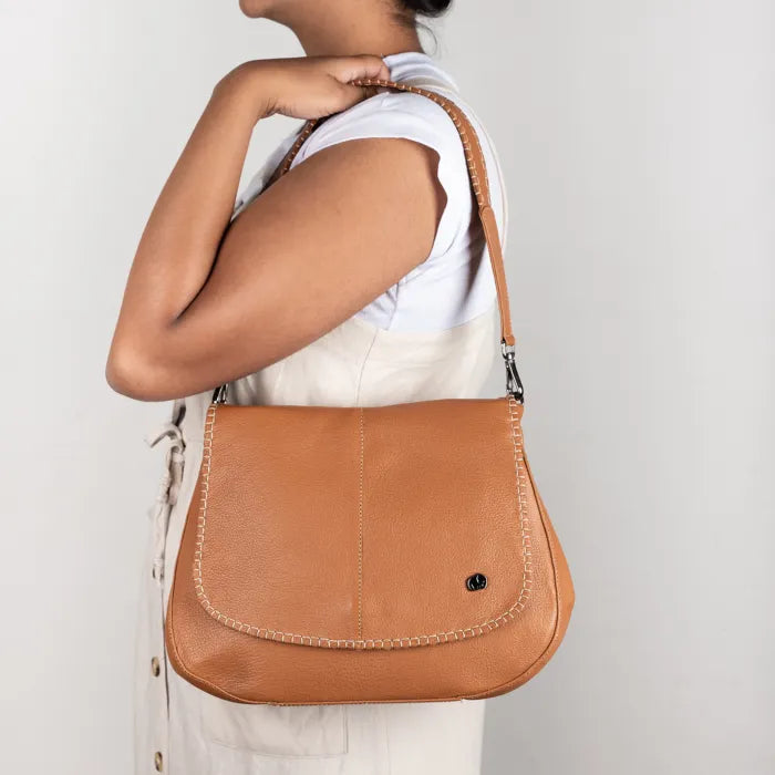 Person wearing a tan leather shoulder bag on a plain background