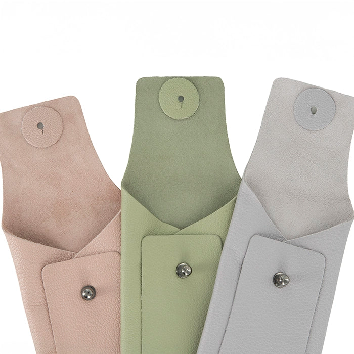 Three leather sunglass cases in pink, green, and grey with buttons on a white background