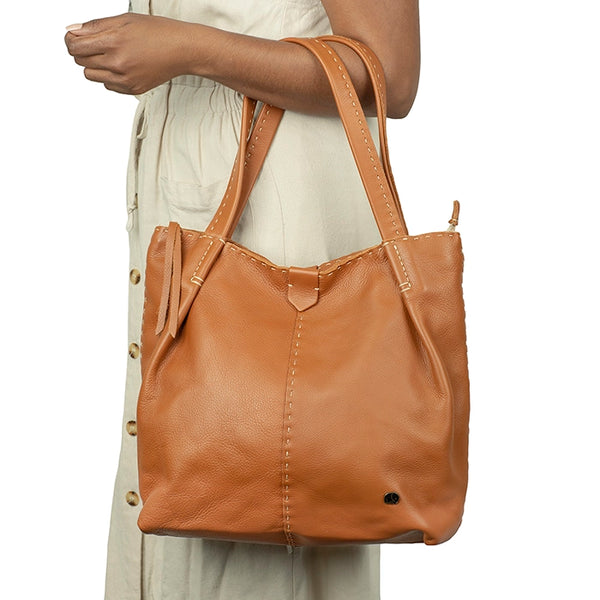 Tan leather handbag held by a person on a white background