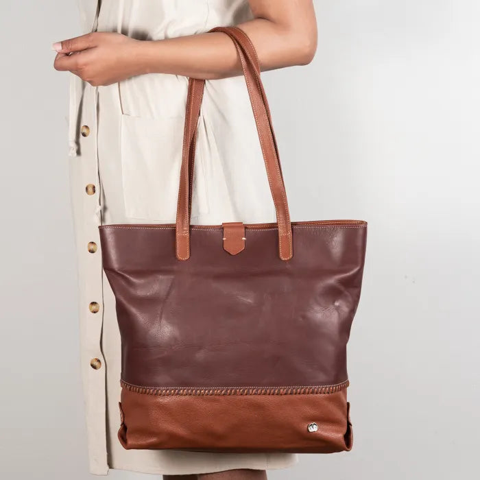 Maroon and Brown leather tote bag held by a person against a plain background