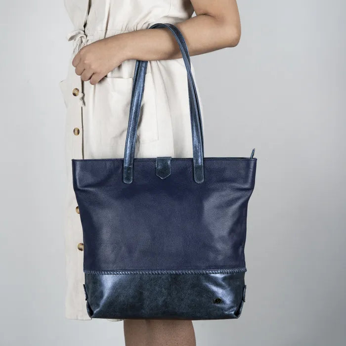Navy blue leather tote bag held by a person against a neutral background
