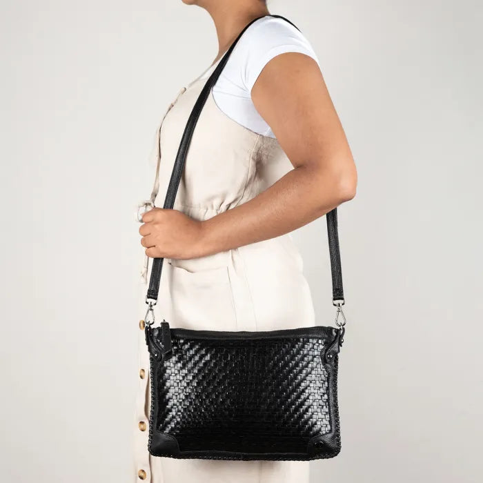 Person holding a black woven handbag against a plain background