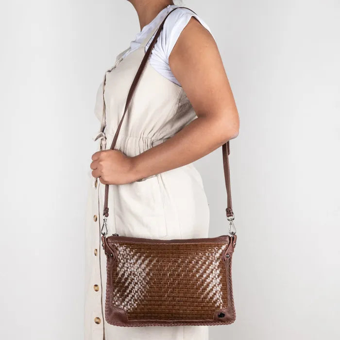 Person holding a brown woven handbag against a white background