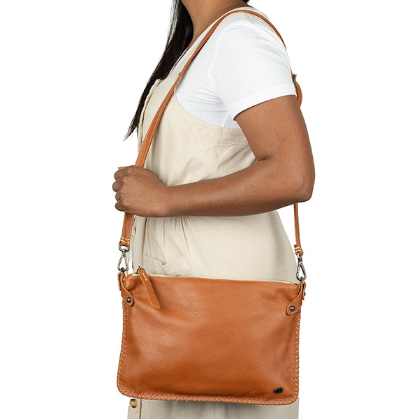 Person wearing a tan leather crossbody bag on a white background