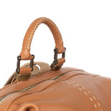 Close-up of a tan leather bag with decorative handle and stitching details on a white background