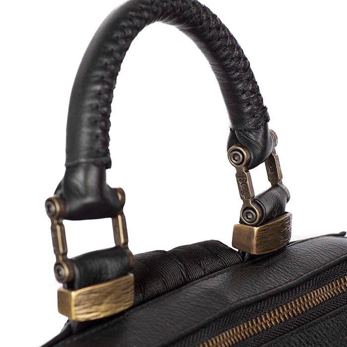 Close-up of a black leather bag handle with brass trims on a white background